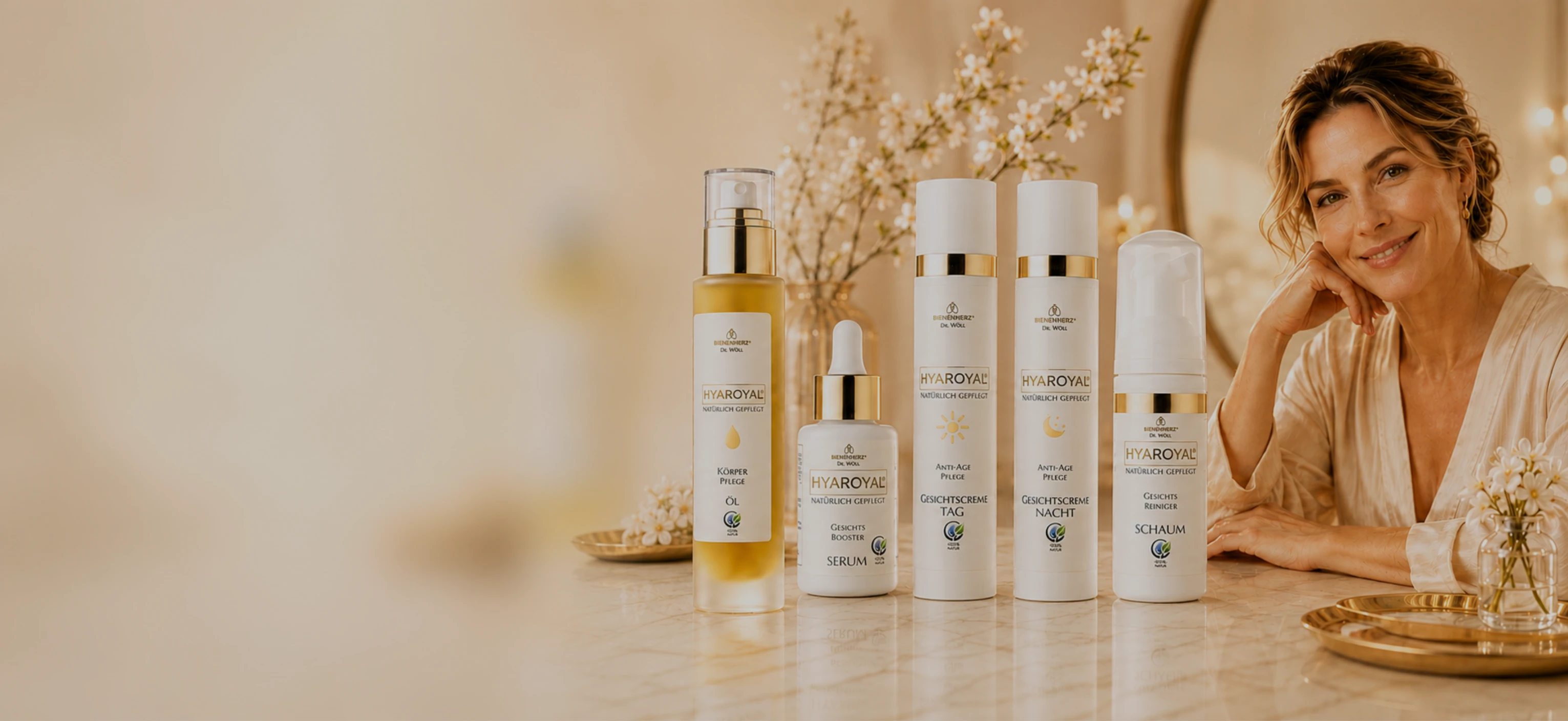 Eine Dame mittleren Alters sitzt in einer luxuriösen SPA-Umgebung. Im Vordergrund stehen einige der HYAROYAL® Produkte von Bienenherz.